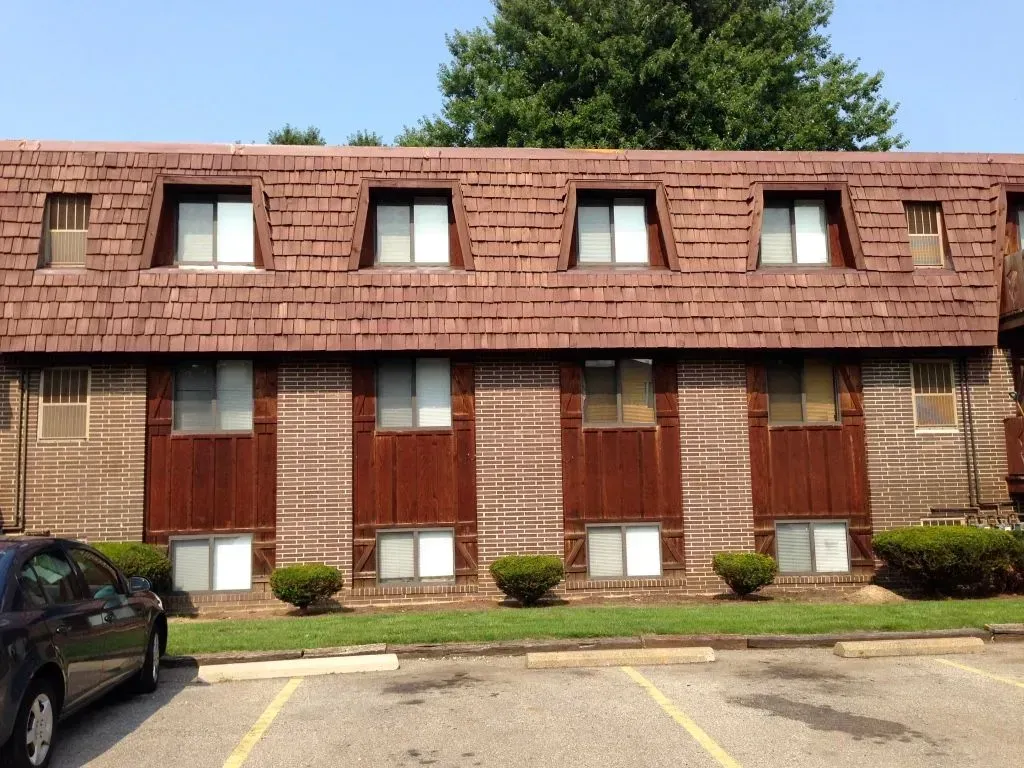 Row of brown brick apartment units with red roof shingles and small windows beside a parking lot