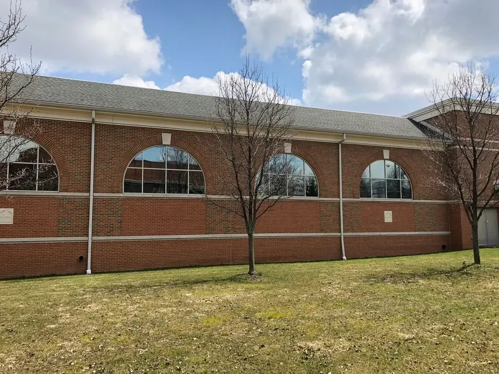Brick building with arched windows, white trim, and leafless trees in front on a grassy lawn.