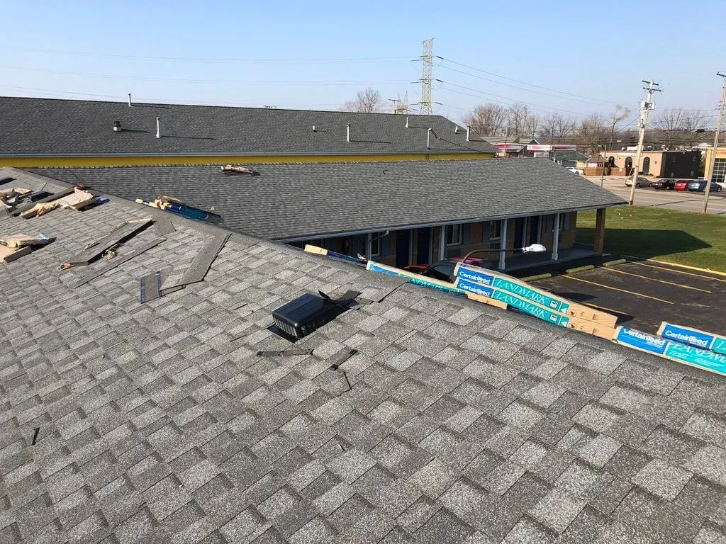 Roof shingles damaged by hail, with a building and blue sky in the background