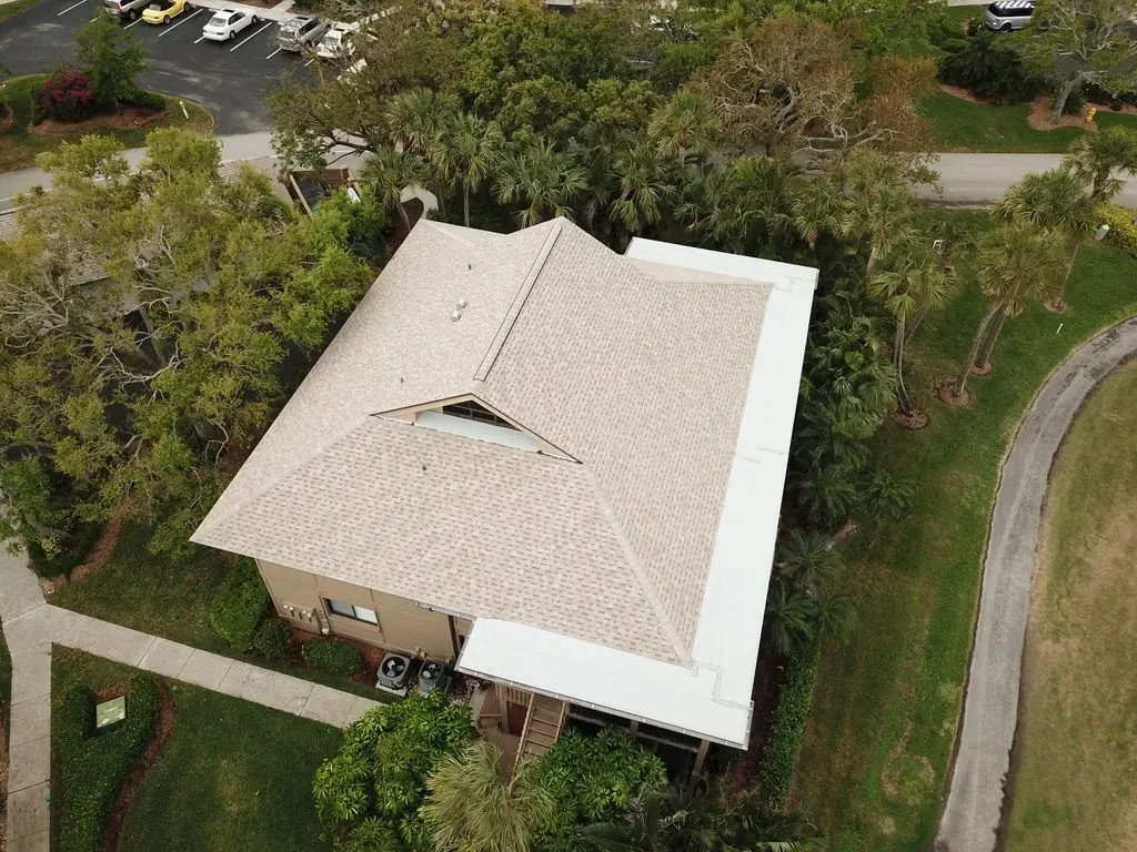 Aerial view of a beige-roofed house surrounded by trees and a driveway.
