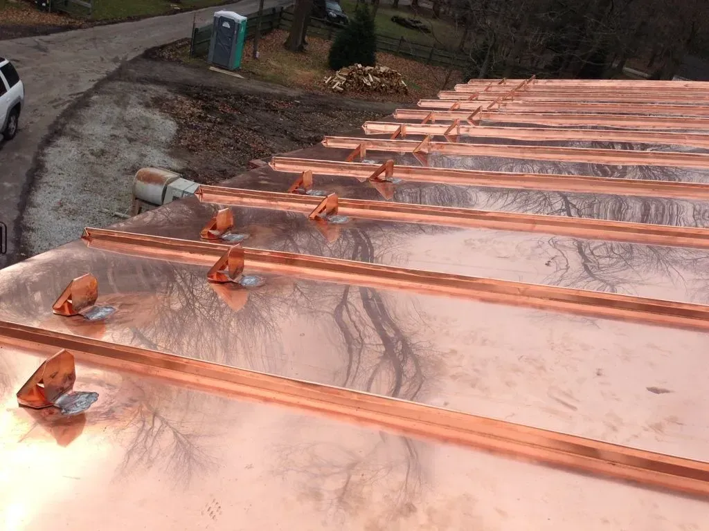 Copper metal roofing panels being installed, with rows of shiny sheets and fasteners on a sloped roof.