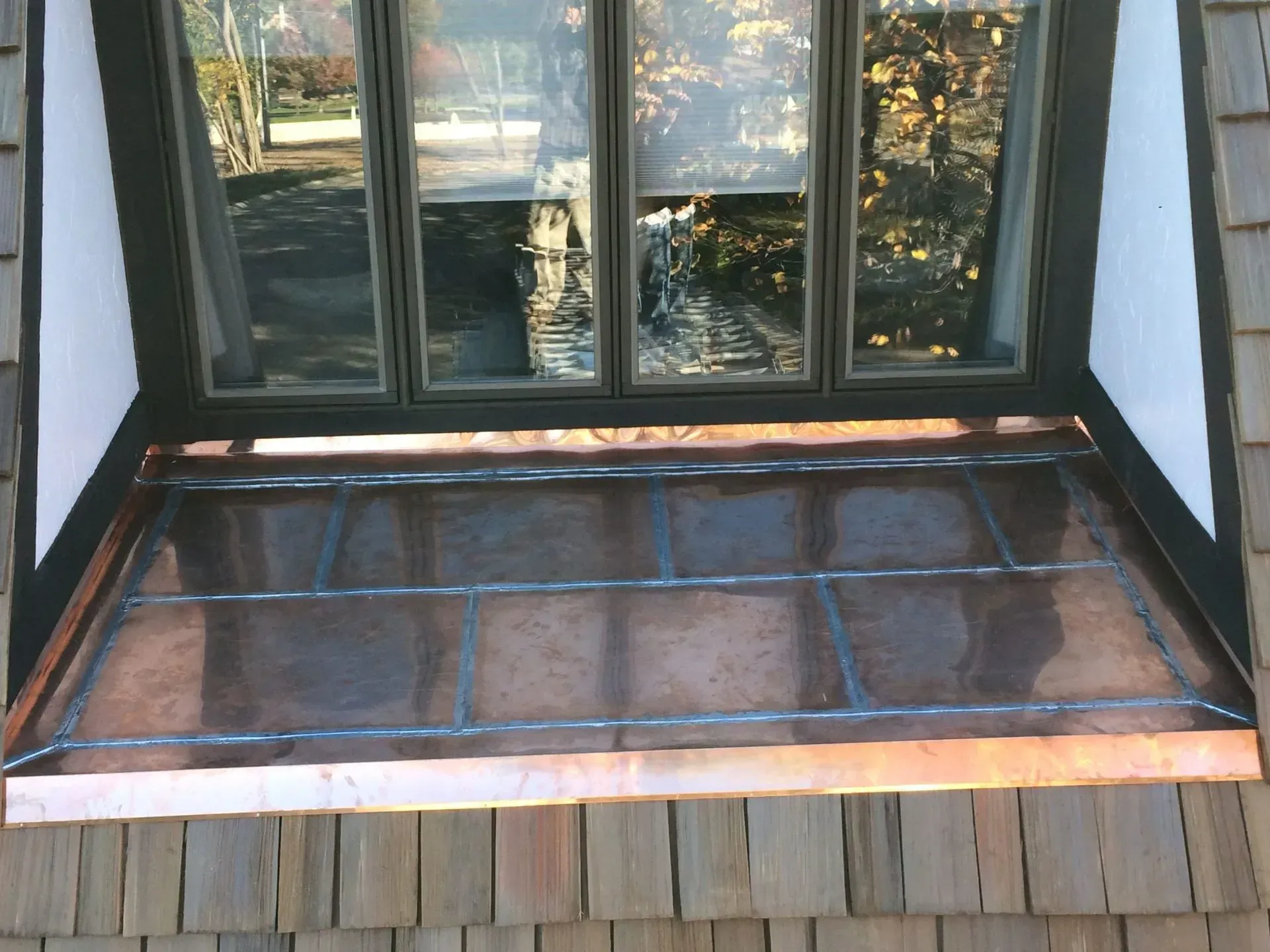 Small wooden balcony with a dark roofed cover and glass doors behind it.