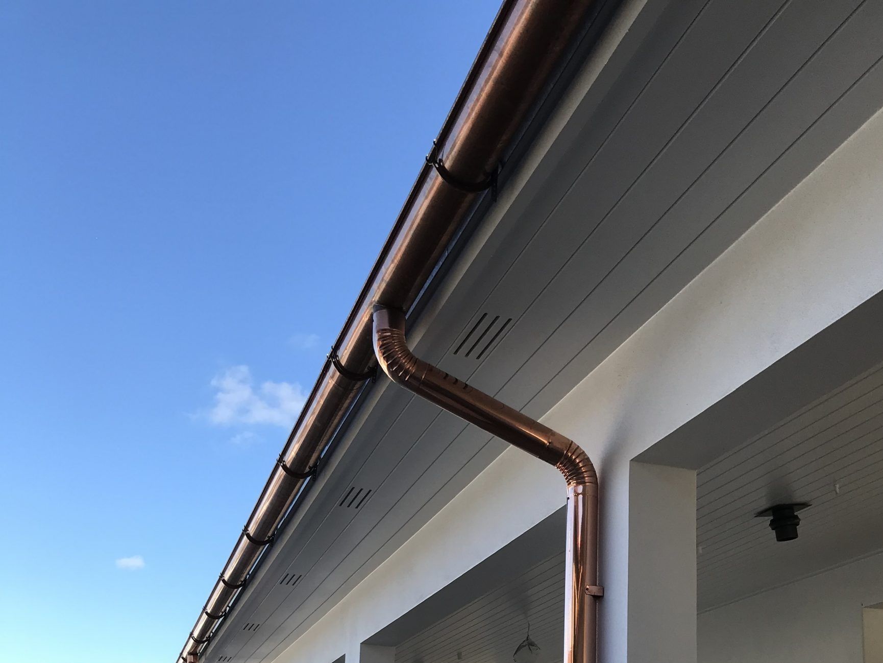 Brown rain gutter on a white house roof against a blue sky