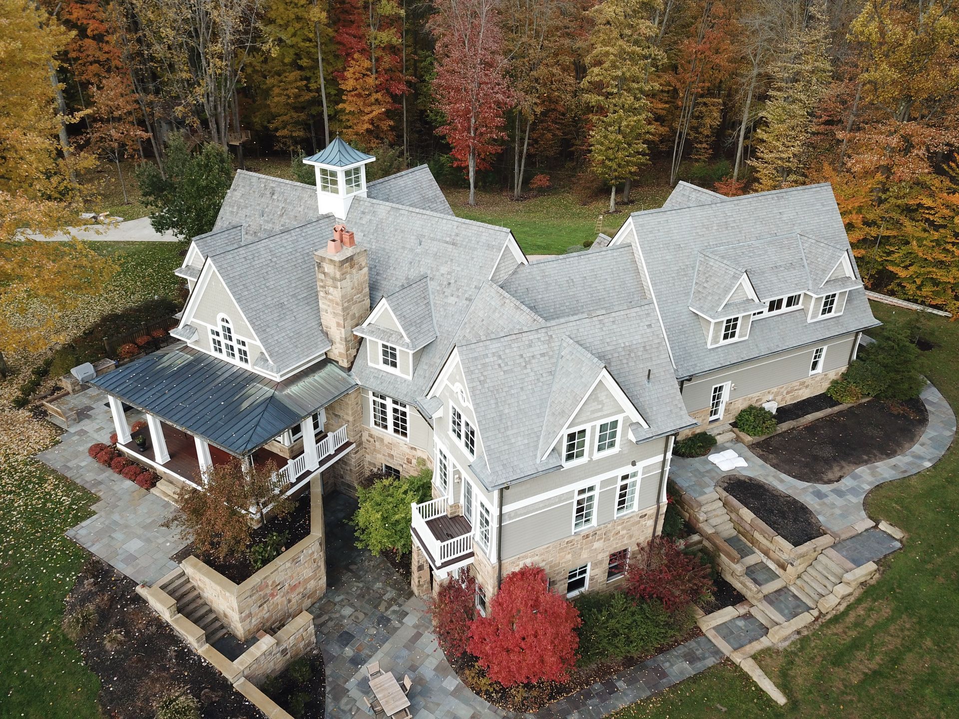 Aerial view of a large gray house with autumn trees and landscaped grounds