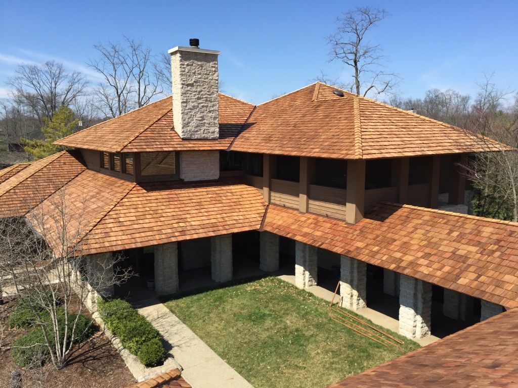 Two-story house with orange tile roof, stone chimney, and courtyard under a blue sky