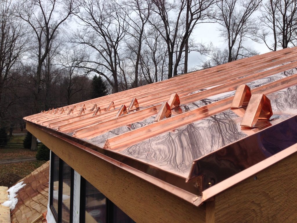 Copper roof with standing seams and snow patches on a house, with bare trees in the background