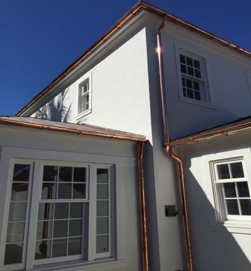 White two-story house exterior with copper gutters, large windows, and a blue sky overhead