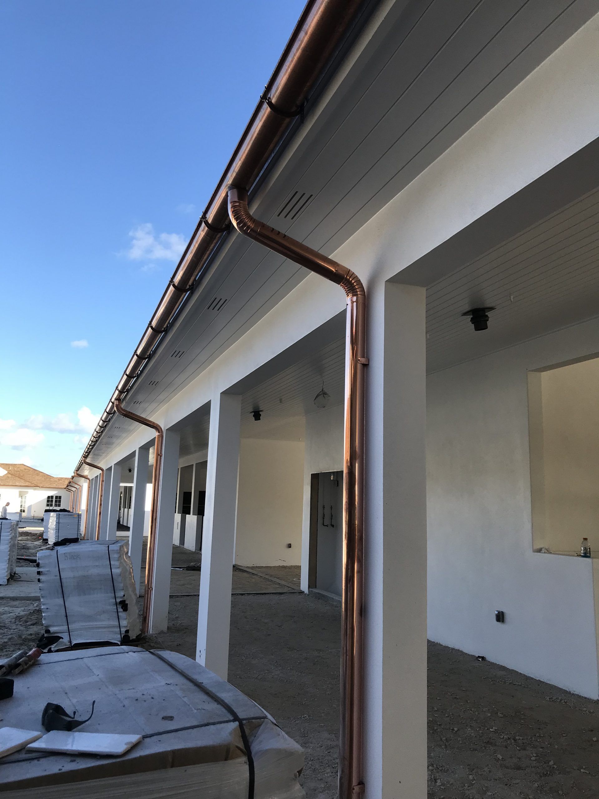 Open patio with white columns, brown gutter, and construction materials along a building exterior