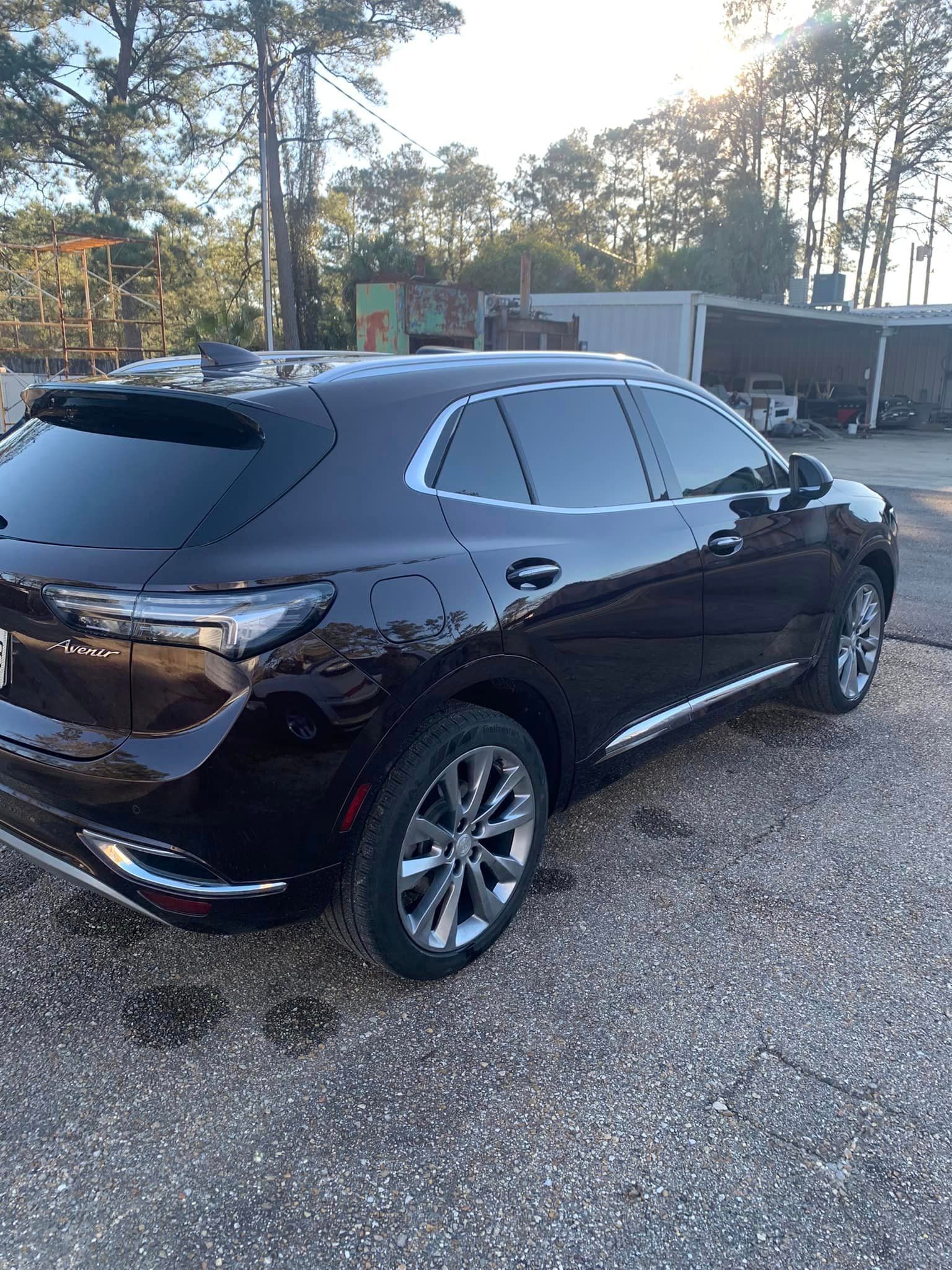 a black car is parked in a gravel lot in front of a building .