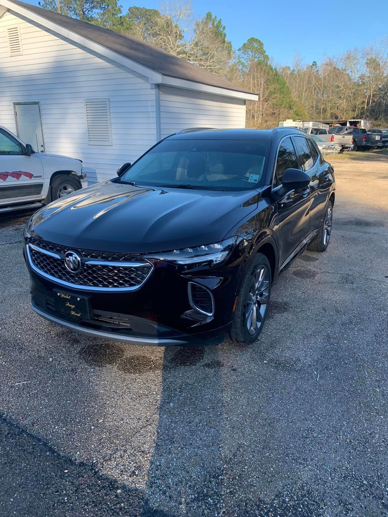 a black car is parked in a gravel lot in front of a building .