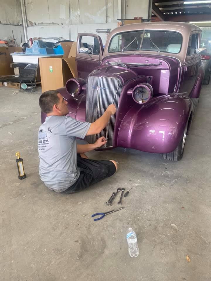 a man is kneeling down next to a purple car in a garage .