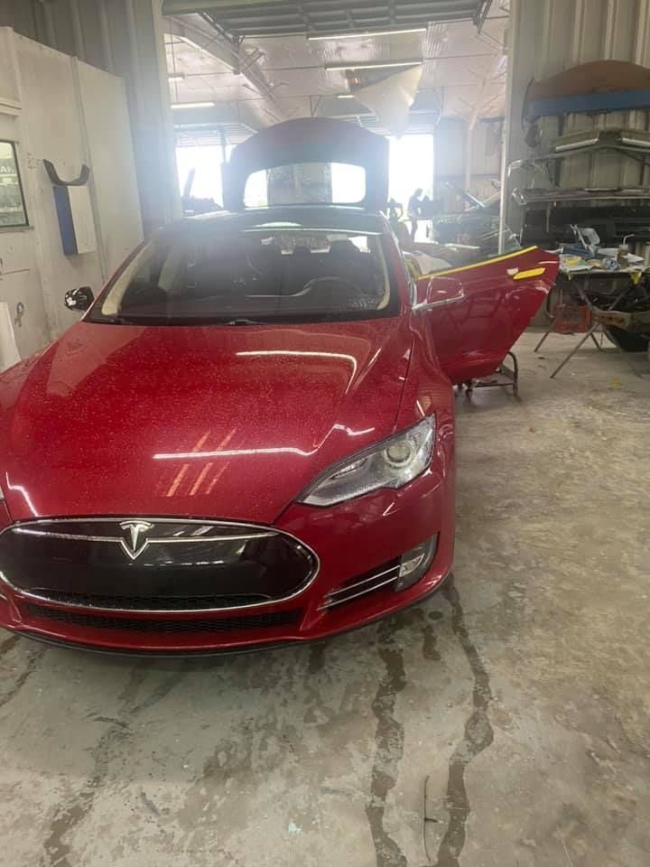 a red tesla model s is parked in a garage with its doors open .