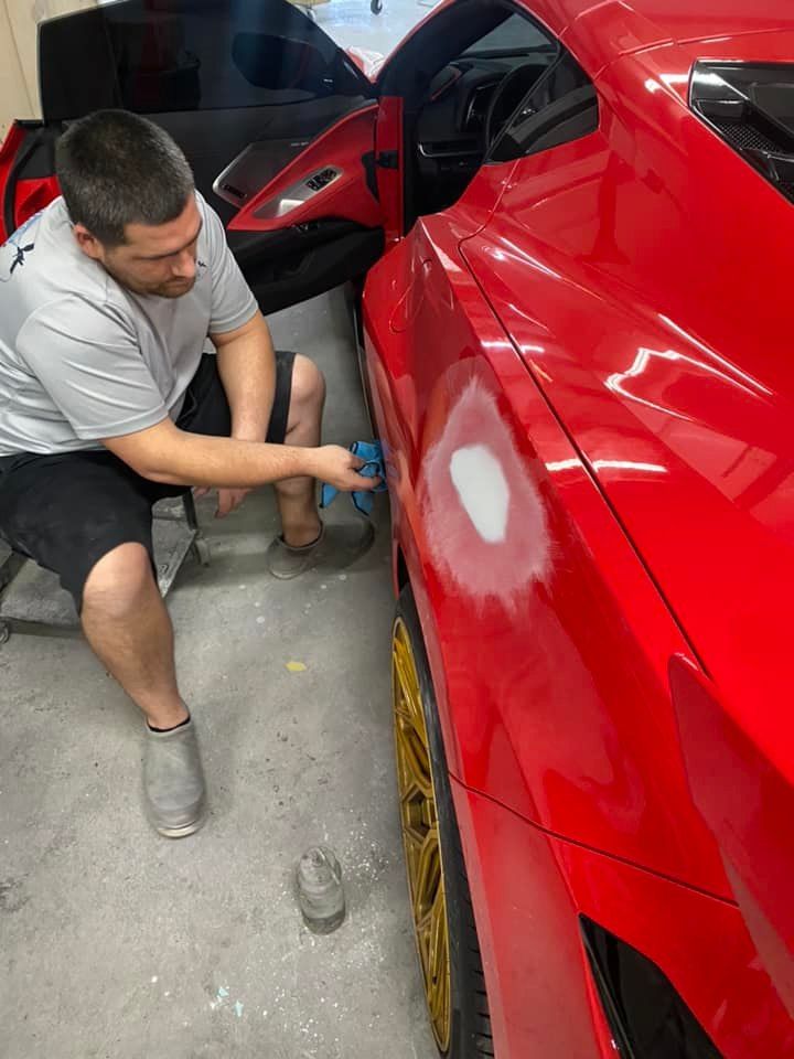 a man is working on a red sports car in a garage .