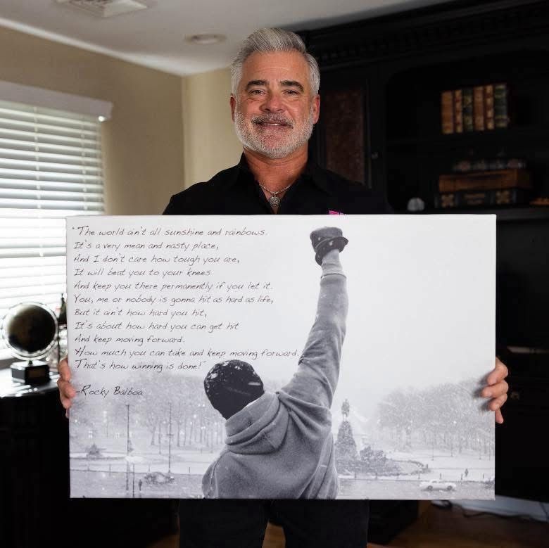 Man holding a large poster with a black-and-white boxing scene and handwritten quote text indoors