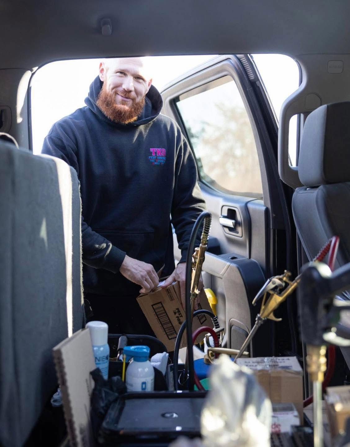 Man standing by an open car door, loading tools and boxes into the back seat area