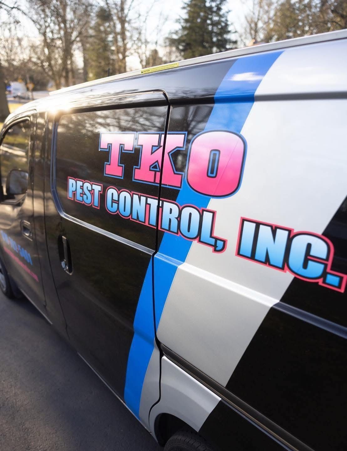 Side of a black pest control van with pink and blue “TKO Pest Control, Inc.” lettering