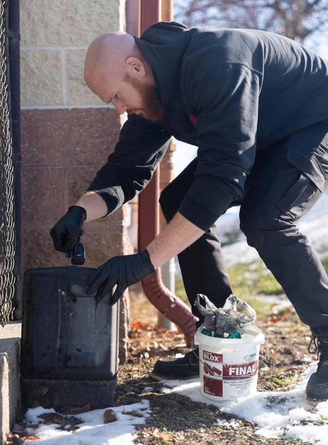 Person bending over a black utility box beside a bucket on a snowy sidewalk