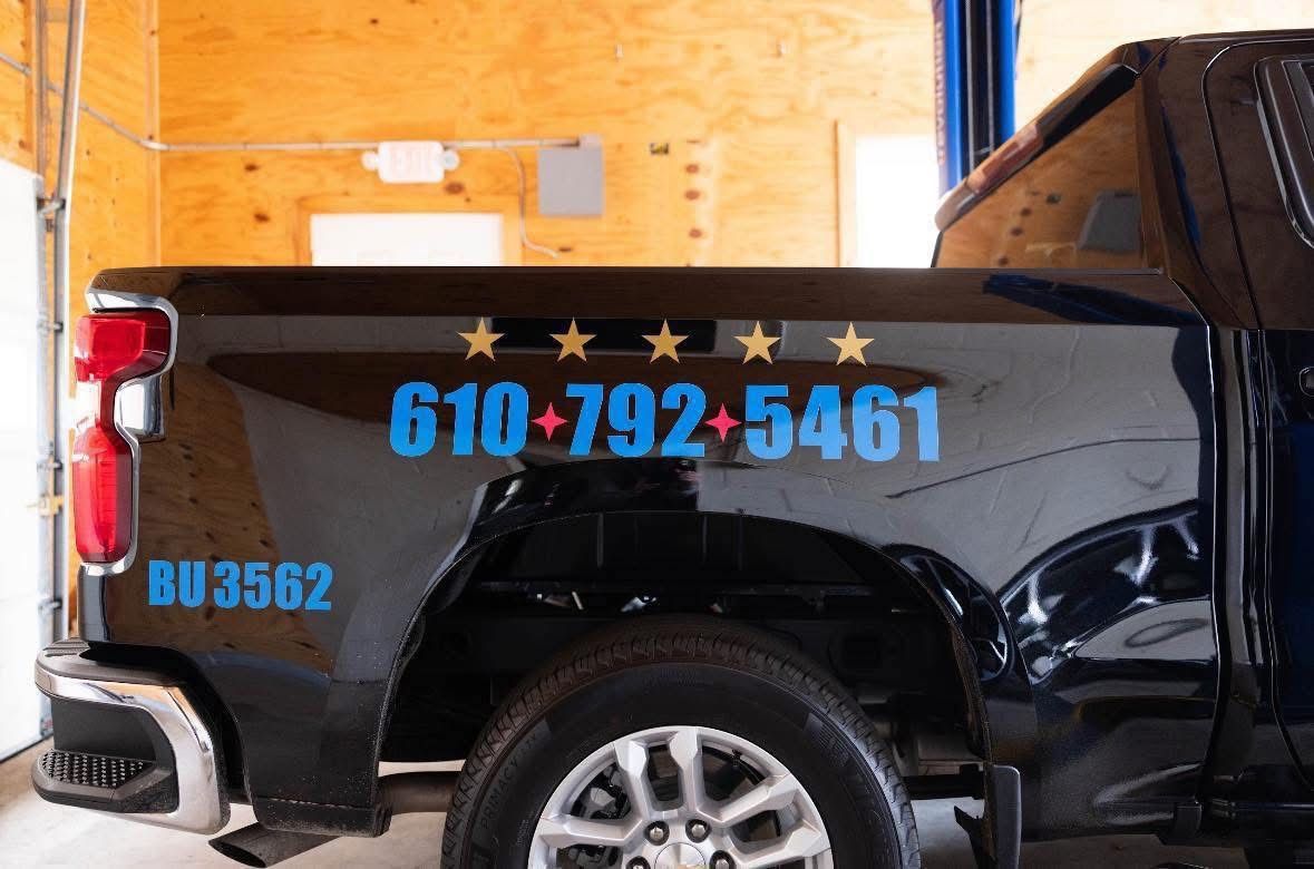 Black pickup truck with blue phone number and “BU3562” on the side in a garage