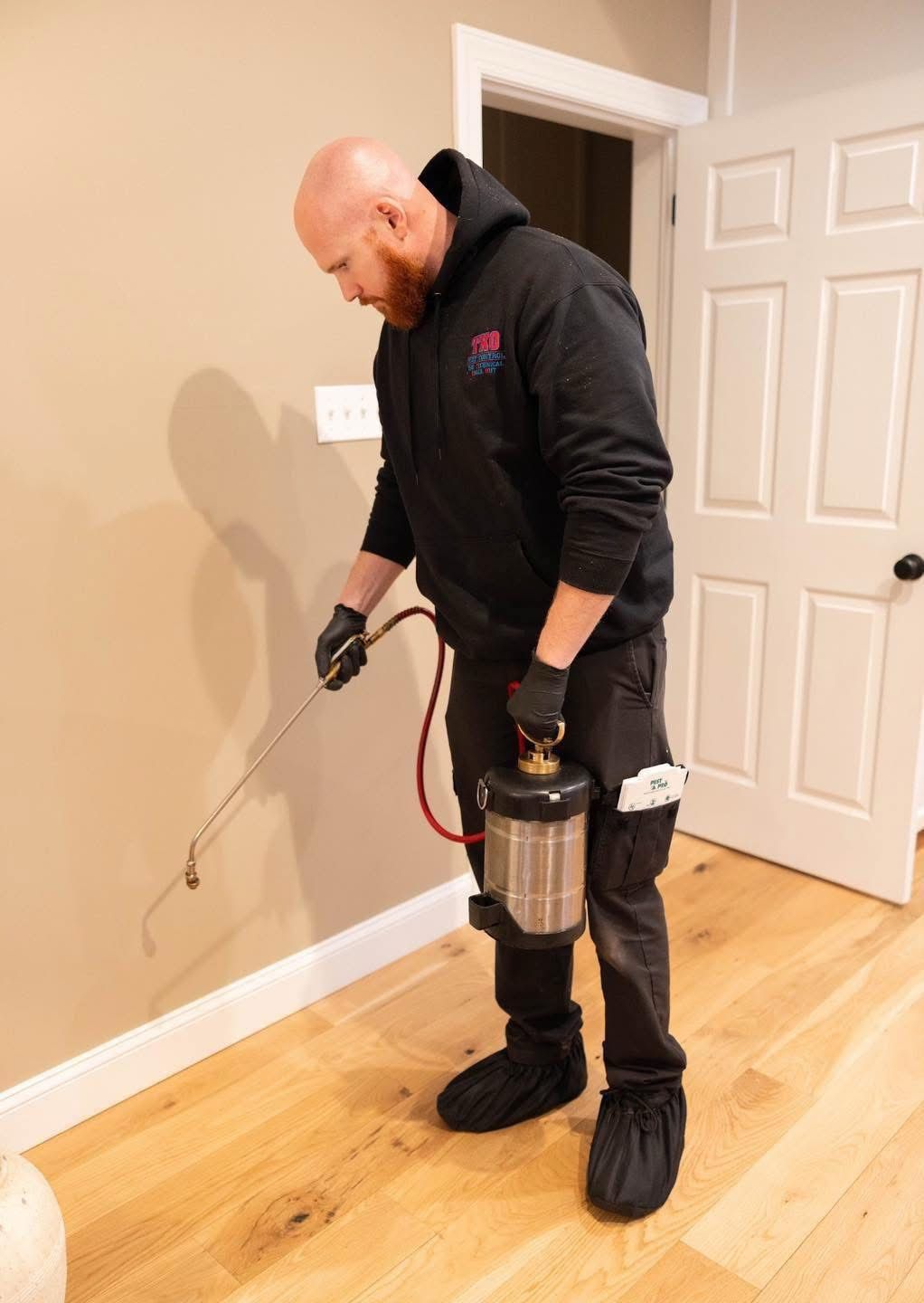 Technician using a spray rig to treat baseboards in a room with wood floors and white doors