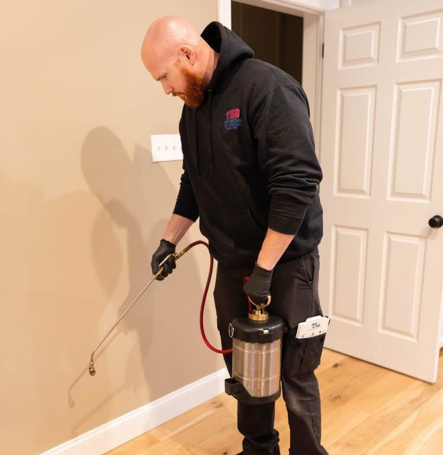 Technician using a pest spray canister and wand inside a home near a wall and doorway