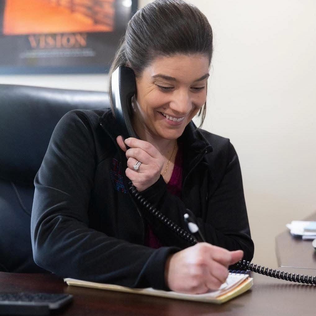 Woman smiling while taking notes on a corded phone in an office setting