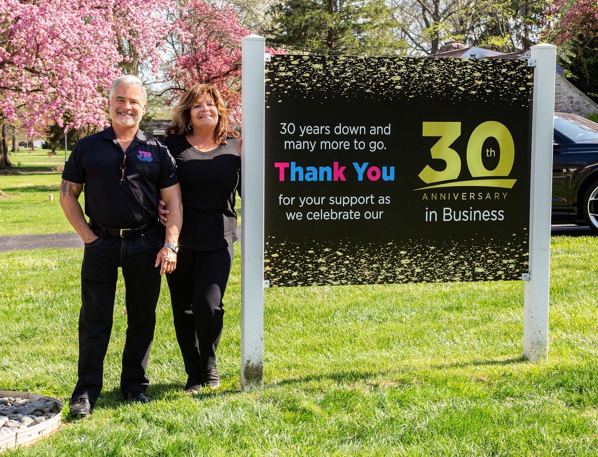 Two people standing beside a sign celebrating 30 years in business in a grassy park