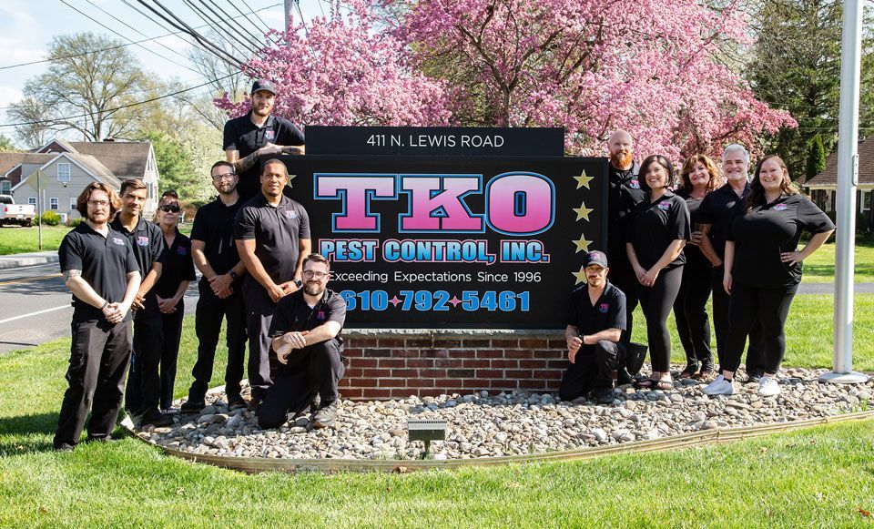 Group posing beside TEKO sign in front of pink flowering trees on a sunny day