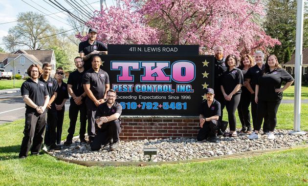 Group posing beside TEKO sign in front of pink flowering trees on a sunny day
