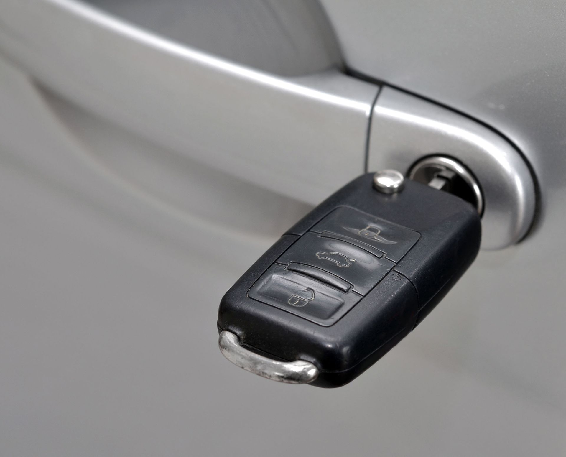 Car key inserted in the door handle lock on a silver car.