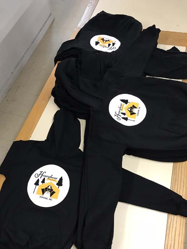 A stack of black hoodies with a yellow logo on them