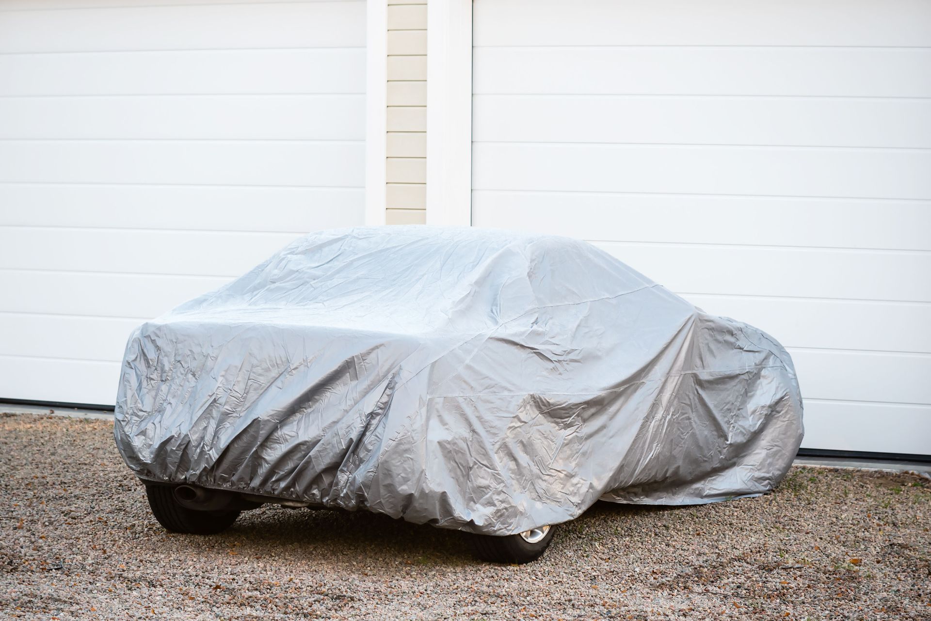 Car covered with a silver tarp parked in front of white garage doors