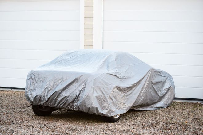 Car covered with a silver tarp parked in front of white garage doors