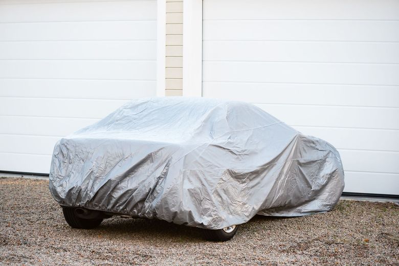 Car covered with a silver tarp parked in front of white garage doors