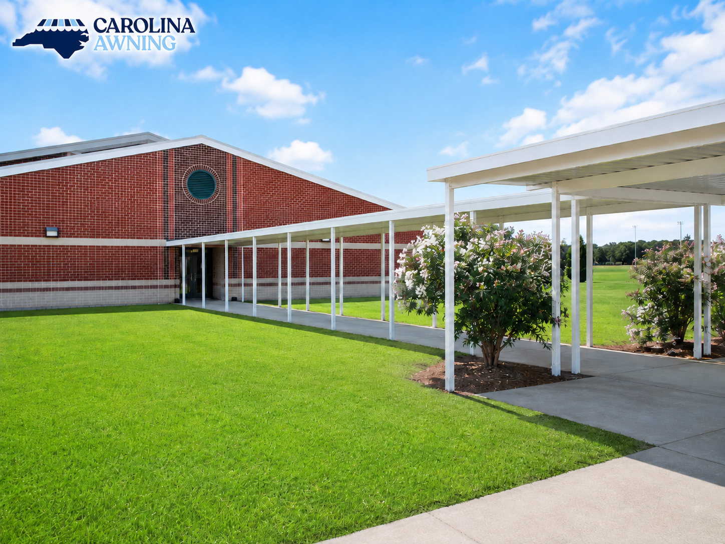 School building with red brick walls, white canopy walkway, and green lawn under a blue sky