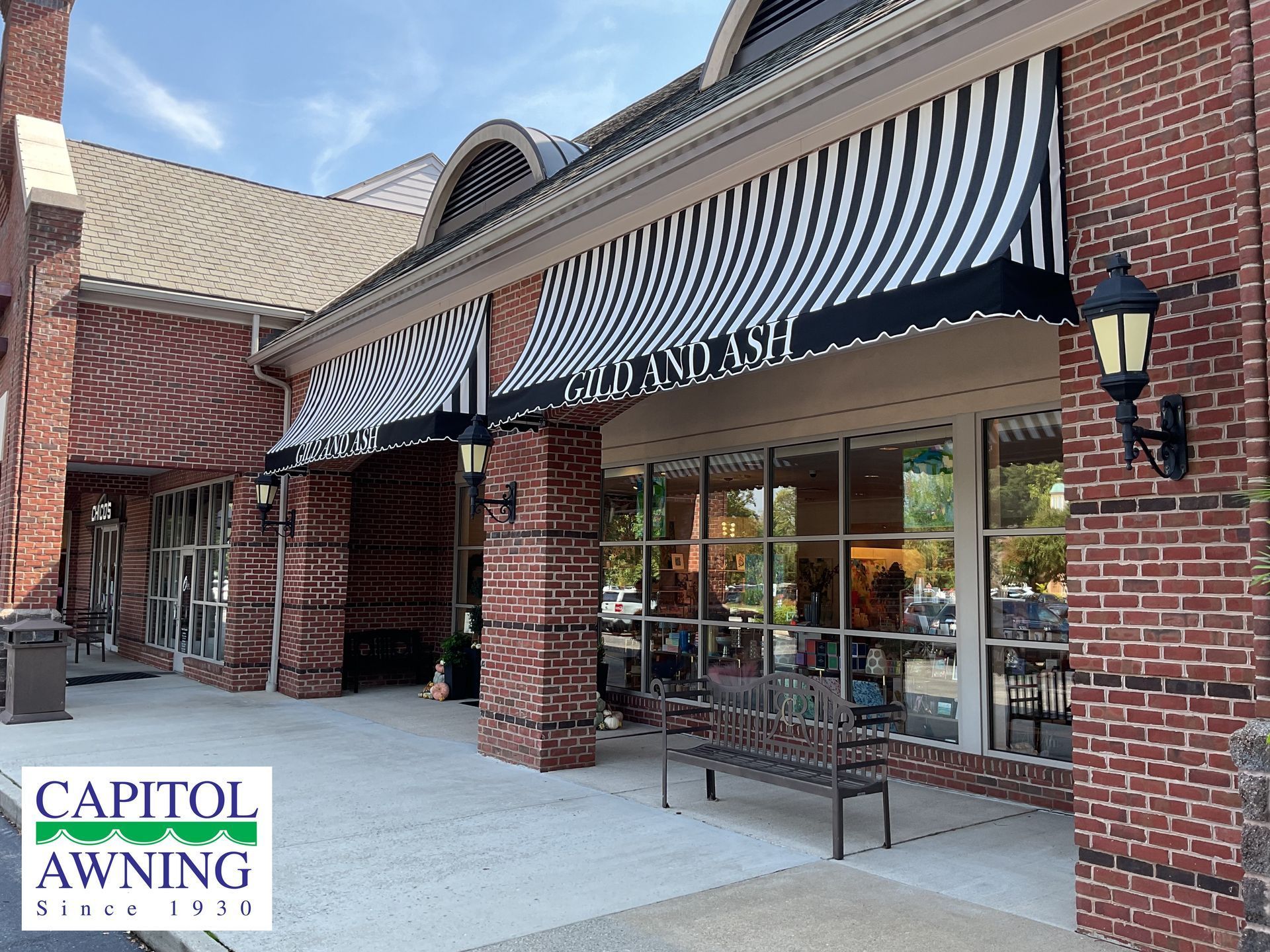 Storefront with black-and-white striped awning and brick columns on a sunny sidewalk.