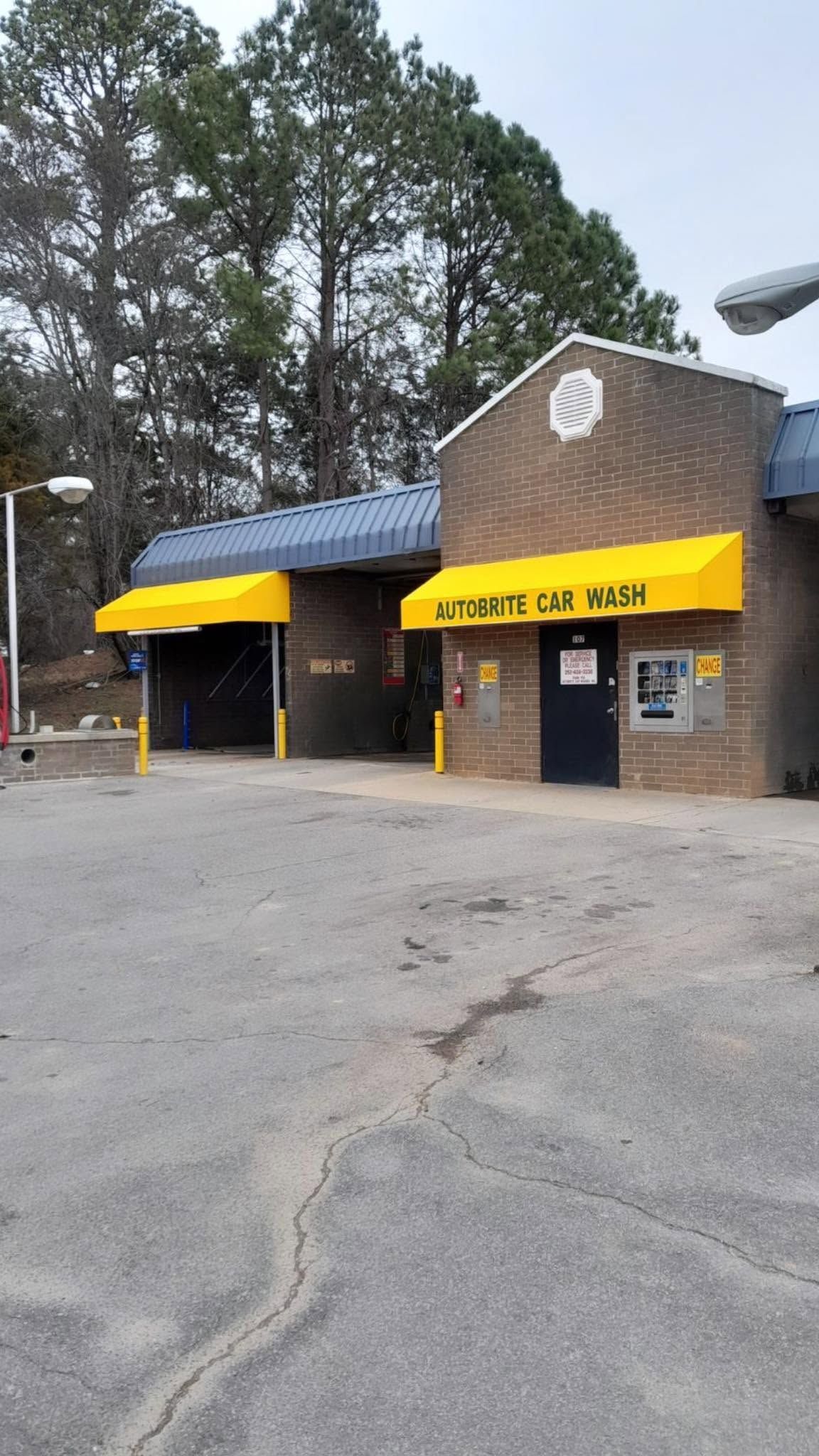 Small brick building with yellow awnings and a front entrance, surrounded by trees and an empty parking lot.