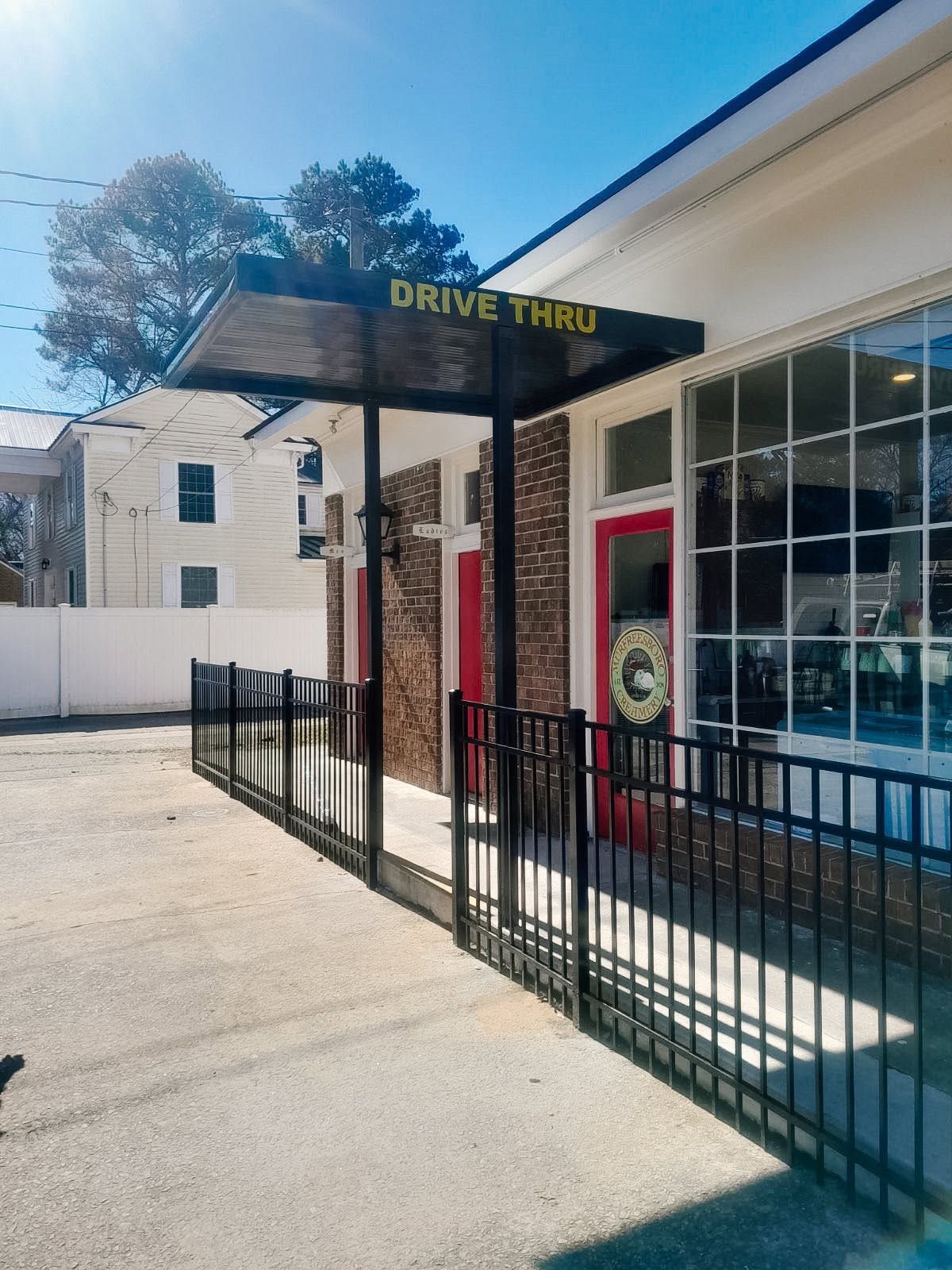 Exterior of a drive-thru restaurant with a black fence, red door, and large windows on a sunny day