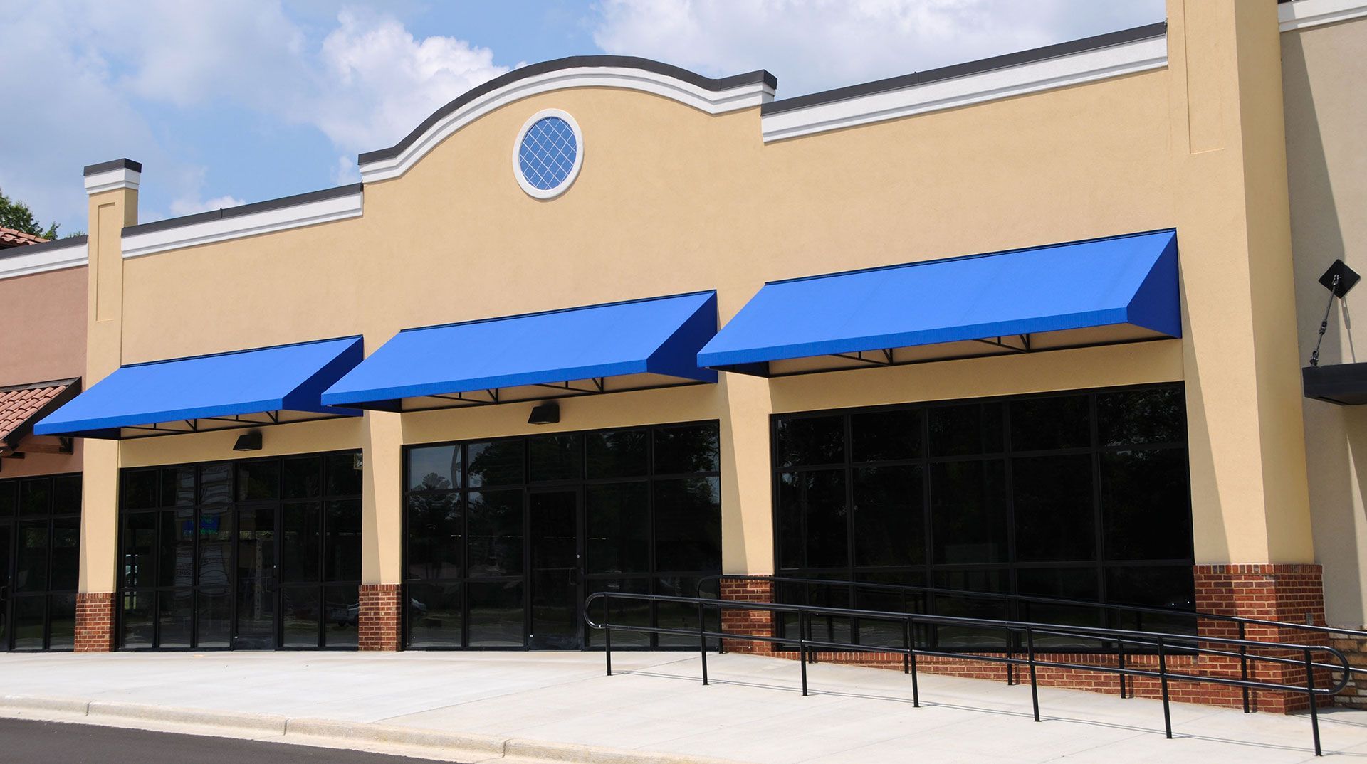 Tan storefront with blue awnings and large windows under a pale sky