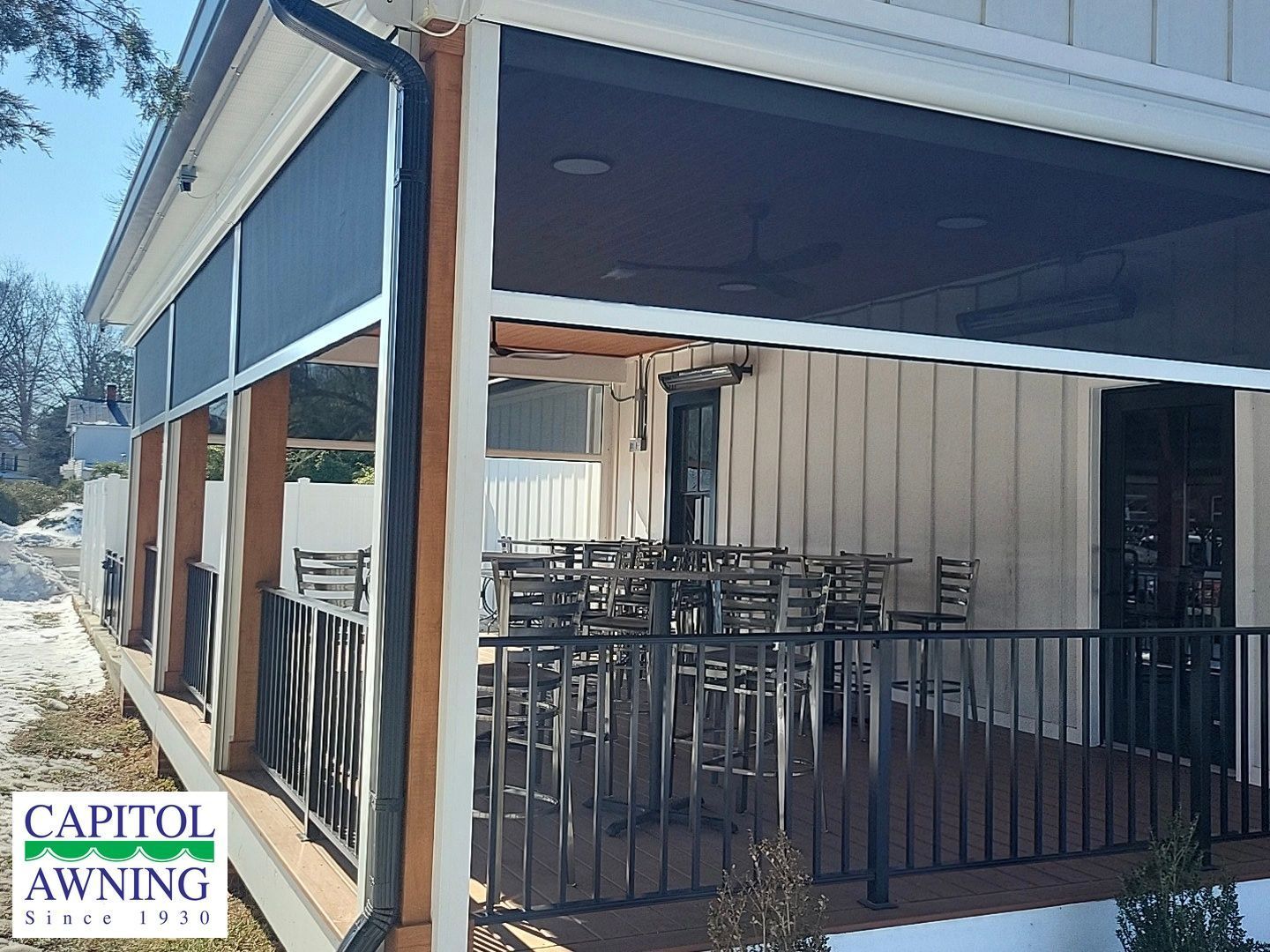 Outdoor restaurant patio with stacked chairs under a blue awning and black railing