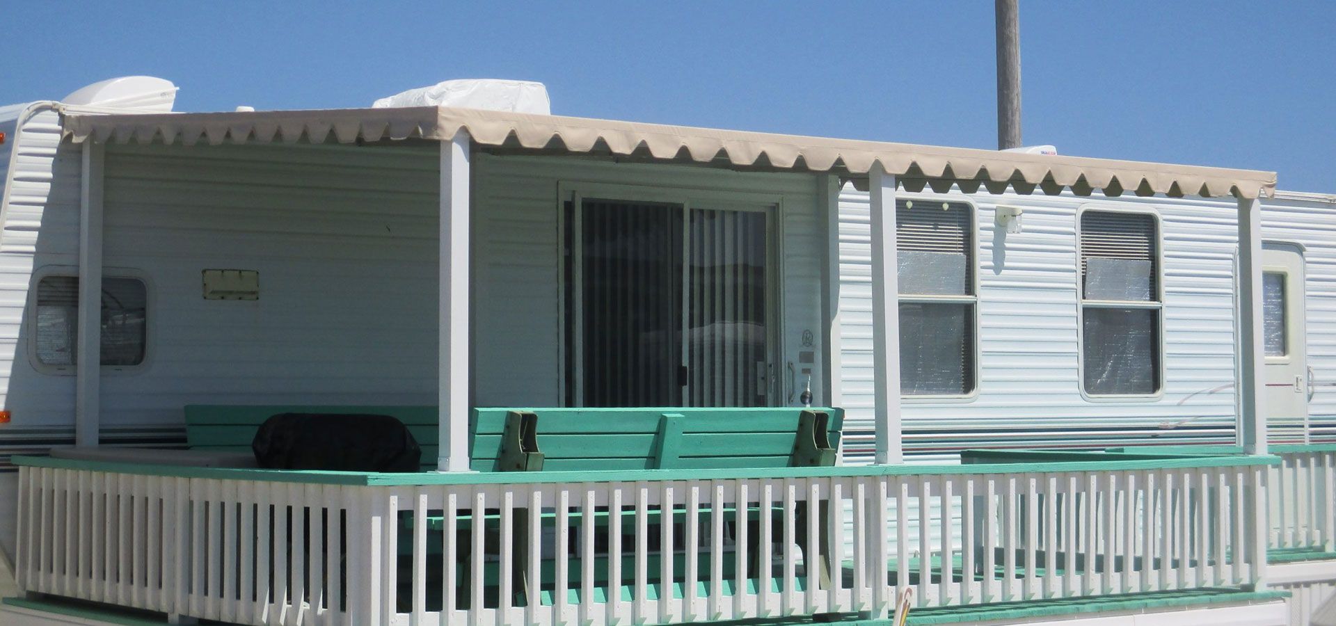 White mobile home with teal porch and white fence under a clear blue sky