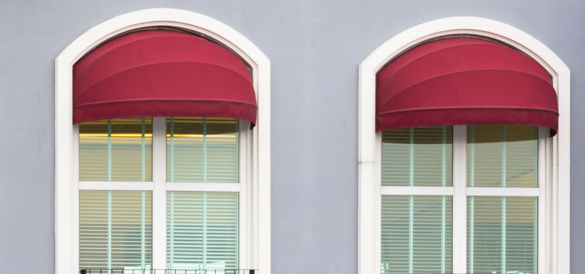 Two red window awnings over white-framed windows on a gray building facade