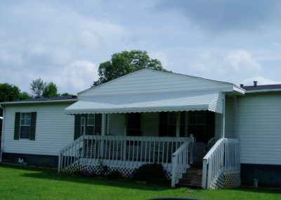 White house with a covered front porch, steps, and green lawn under a cloudy sky
