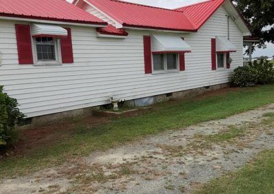 White house with a red metal roof and red shutters beside a gravel driveway.