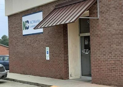 Brick building entrance with striped awning and a sign beside the door