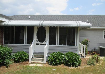 Front porch of a beige house with white railings, steps, and a covered awning
