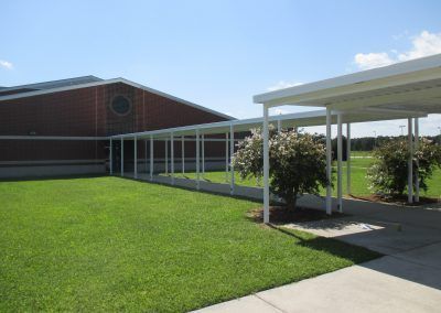 School building with covered walkway, green lawn, and clear blue sky