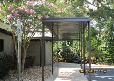 Covered walkway beside a building, with pink flowering tree and green landscaping