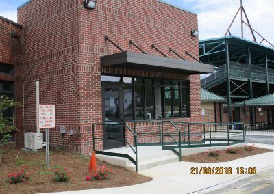Brick building entrance with black awning, railing ramp, and metal stairs beside it.