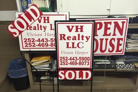 Realty office signs for VH Realty LLC, red and white, with sold and for lease notices on a desk