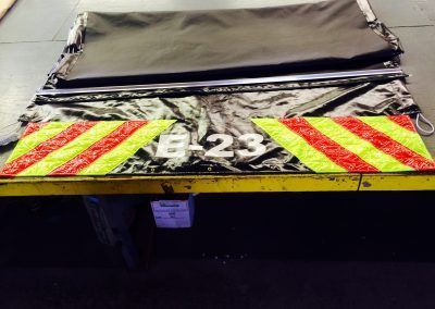Rear of a truck with a torn tarp and red-yellow striped hazard panel marked “E-23”